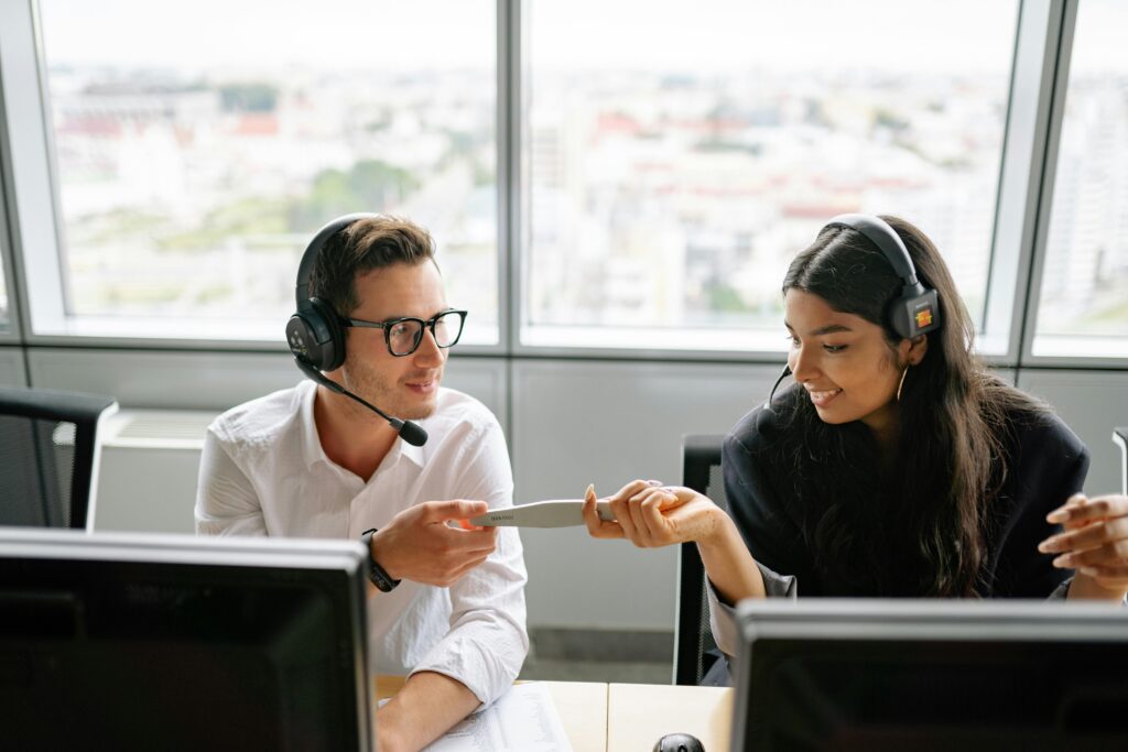 Two call center agents sharing a document while communicating with clients, fostering teamwork.